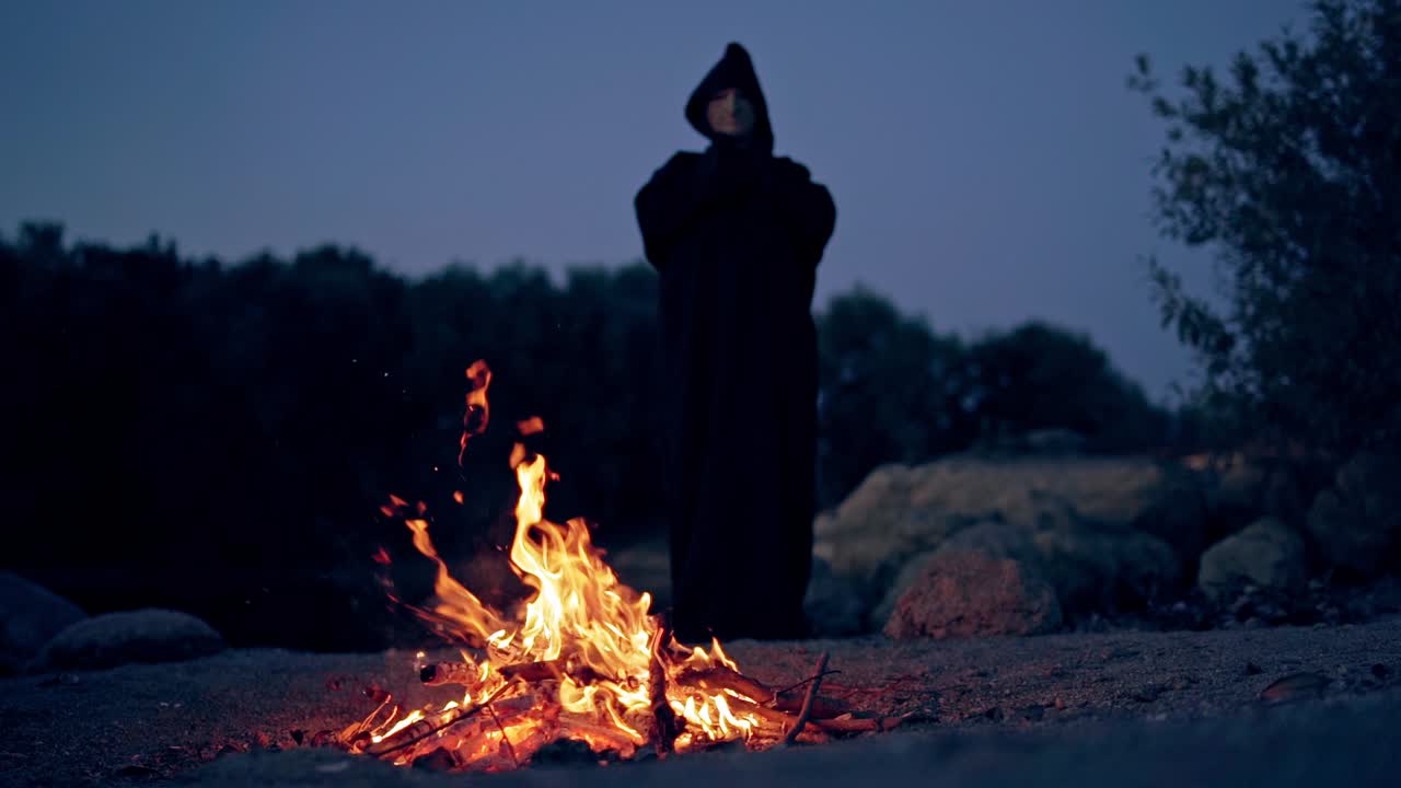 Sad monk by the fire. Man in cassock leans toward the fire at night
