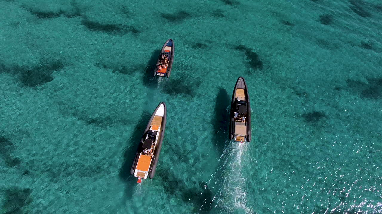 Overhead drone shot of 3 speedboats moving slowly in clear blue water of the sea