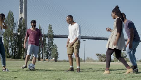 group of five happy friends playing football in park.