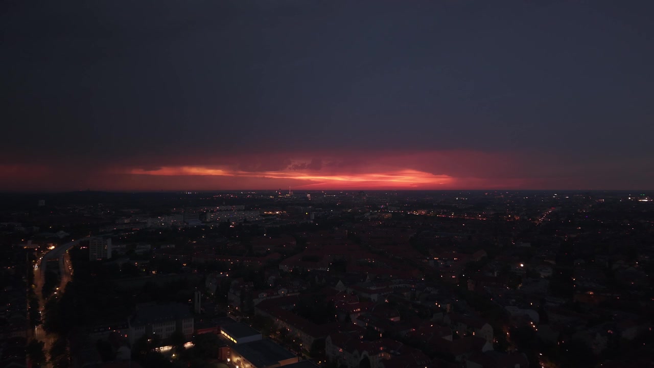 Město s viditelným úderem blesku proti bouřkové obloze, osvětlující noční městskou krajinu. Unikátní letecký pohled, dynamický panoramatický záběr dronem s posunem vpřed.