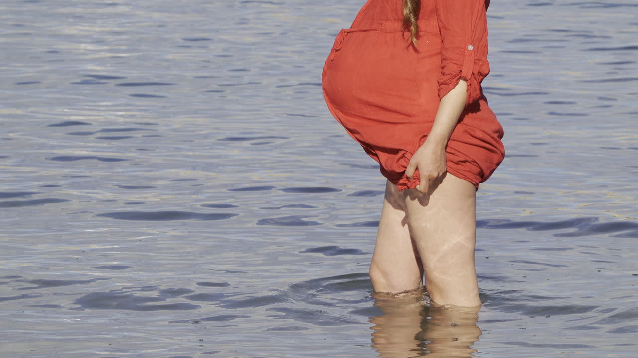 Pregnant woman in a red T-shirt dress and cap moving around in the Mediterranean sea