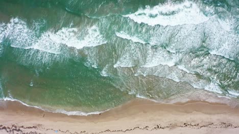 Aerial-drone-shot-slowly-moving-forward-while-looking-down-on-the-beach-with-umbrellas-and-the-waves-crashing-from-the-Atlantic-ocean-on-a-windy-day