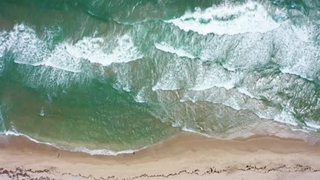 aerial drone shot slowly moving forward while looking down on the beach with umbrellas and the waves crashing from the atlantic ocean on a windy day