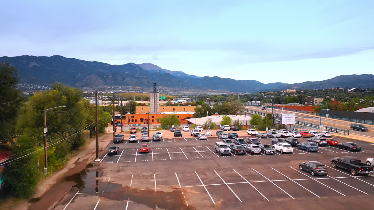 Colorado Springs, USA, 22 July 2025: Rising above the parking lot with half-occupied by the vehicles. Numerous cars ride by the roads of Colorado Springs, Colorado, USA. Mountain range at backdrop