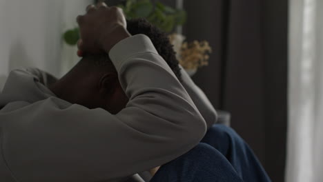 primer plano de un joven con problemas de salud mental sentado en el suelo de su casa junto a la ventana sacudiendo la cabeza pareciendo deprimido e infeliz