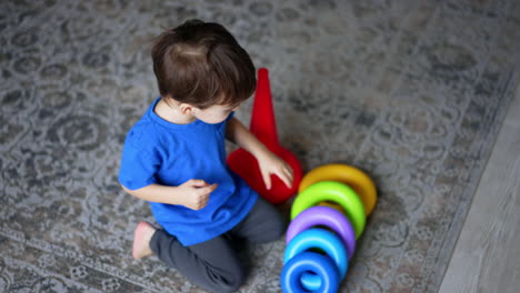 toddler sitting on the floor pulls the basis from toy pyramid. kid starts to build the toy again. top view.