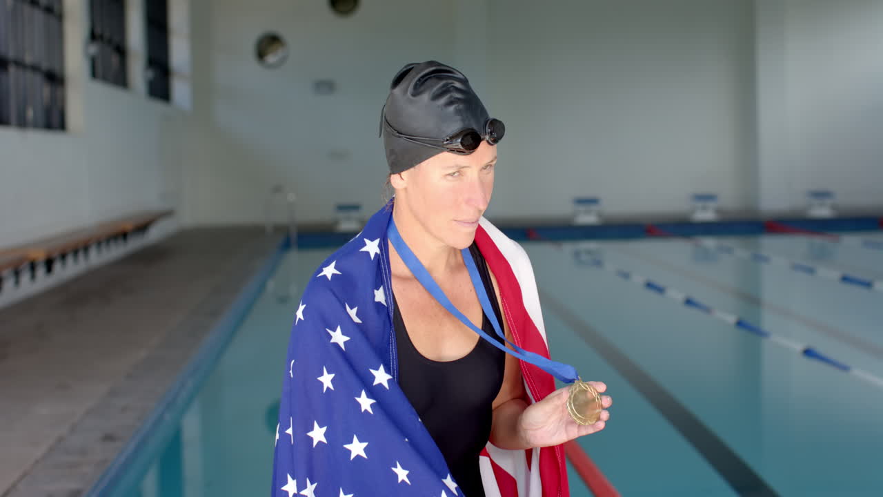 una atleta nadadora caucásica cubierta de bandera estadounidense se encuentra orgullosa a la orilla de una piscina