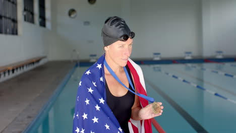 an american flag-draped caucasian female swimmer athlete stands proudly at a poolside