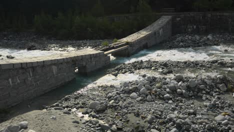 Río-Arroyo-En-Los-Alpes-Italianos-Pasando-Por-El-Antiguo-Puente-De-Piedra,-Alpe-Ventina