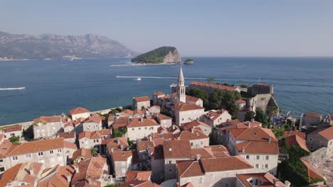 Aerial:-Old-Town-Budva,-Sveti-Ivan-Church-tower,-and-Sveti-Nikola-Island-in-the-background