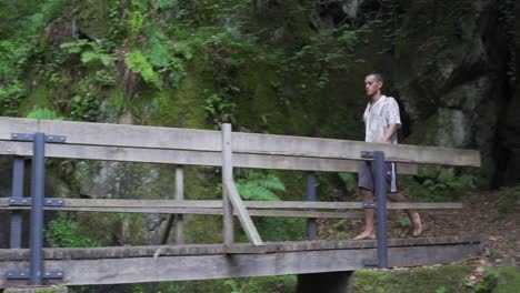 young man walking barefoot over a wooden bridge in the forrest and deeper in the wodds