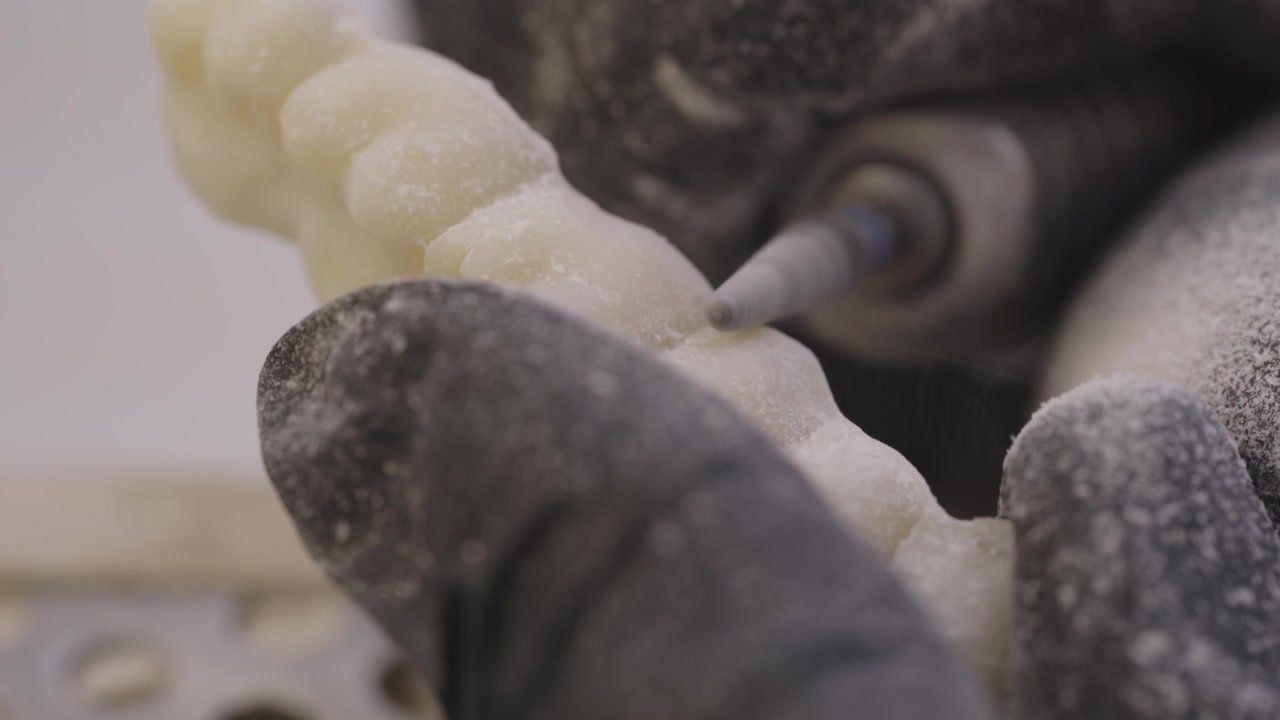 Close up dental technician shaping veneer mold using precision tools in lab setting