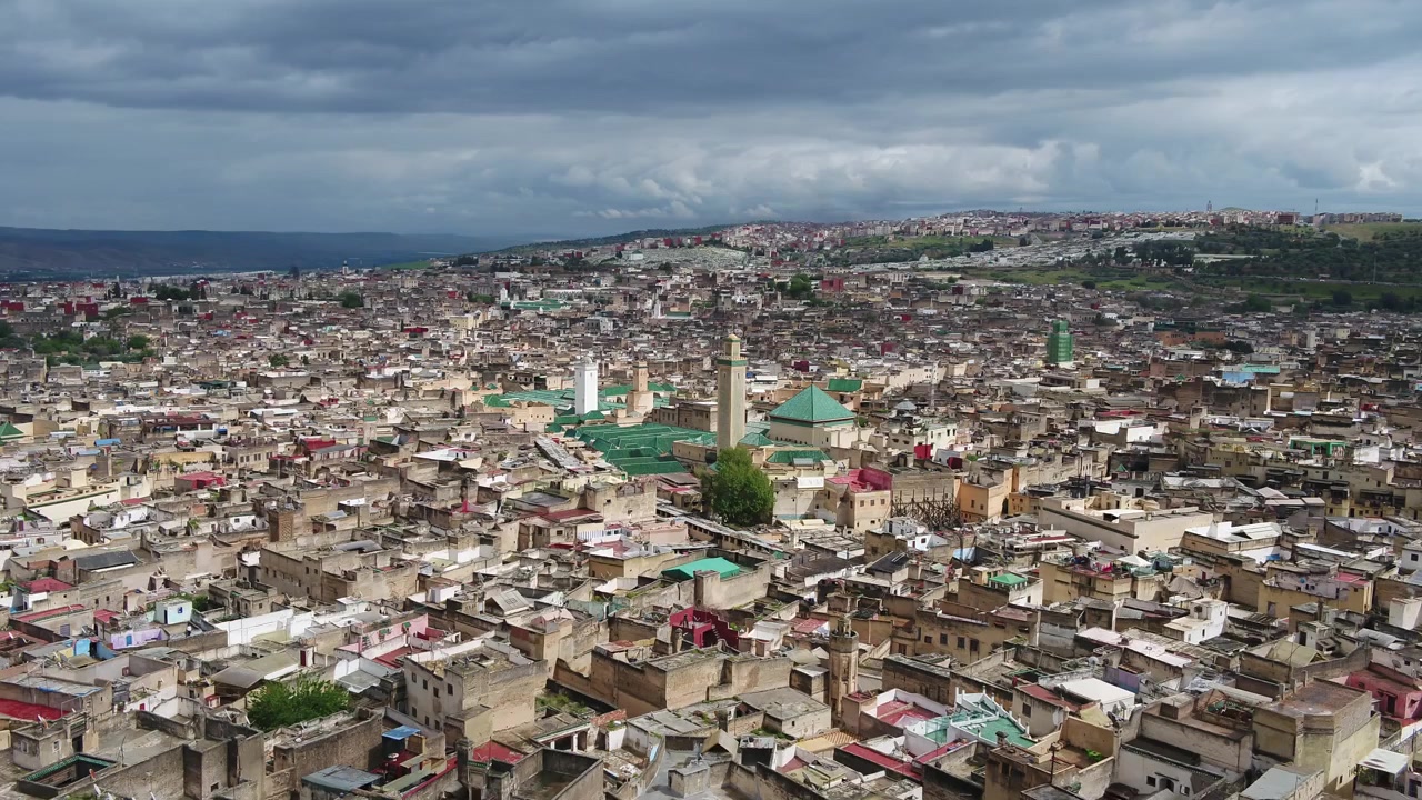 Vista aerea con drone di colline verdi e alberi che si affacciano sul paesaggio urbano storico della Medina di Fez in Marocco, ideale per documentari di viaggio e progetti cinematografici