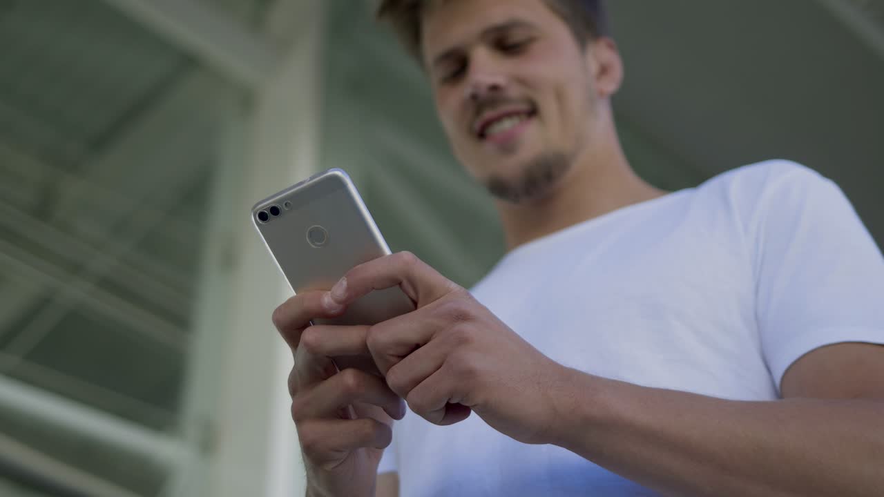 Giovane uomo sorridente che digita un messaggio sullo smartphone