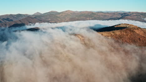 Cloud-covered-mountains-with-peaks-emerging-in-the-sunlight,-aerial-view