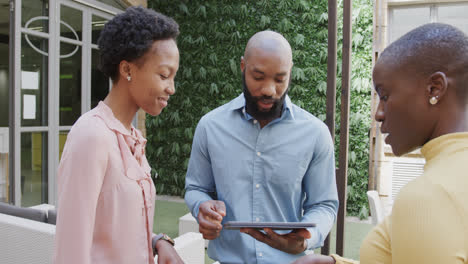 Three-happy-african-american-male-and-female-colleagues-talking-using-tablet-outside,-in-slow-motion