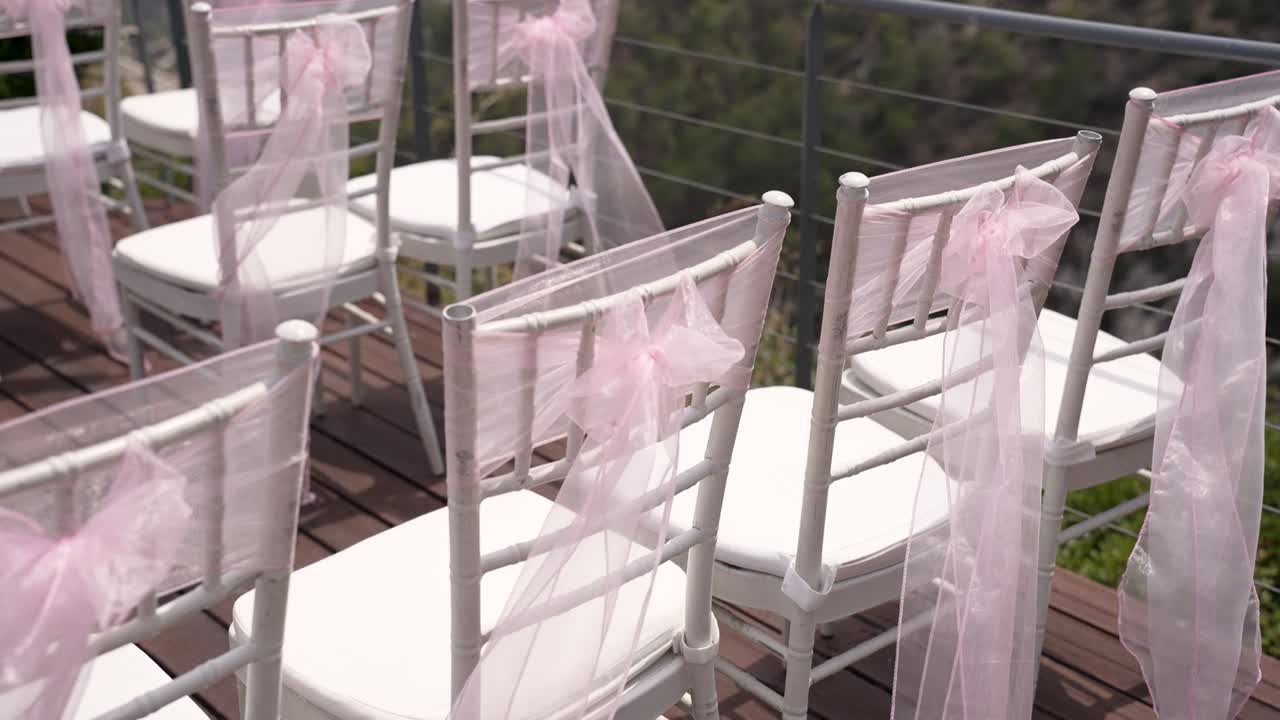 Beautifully arranged chairs with pink ribbons are set for a wedding ceremony, offering a stunning view of the natural landscape in the background