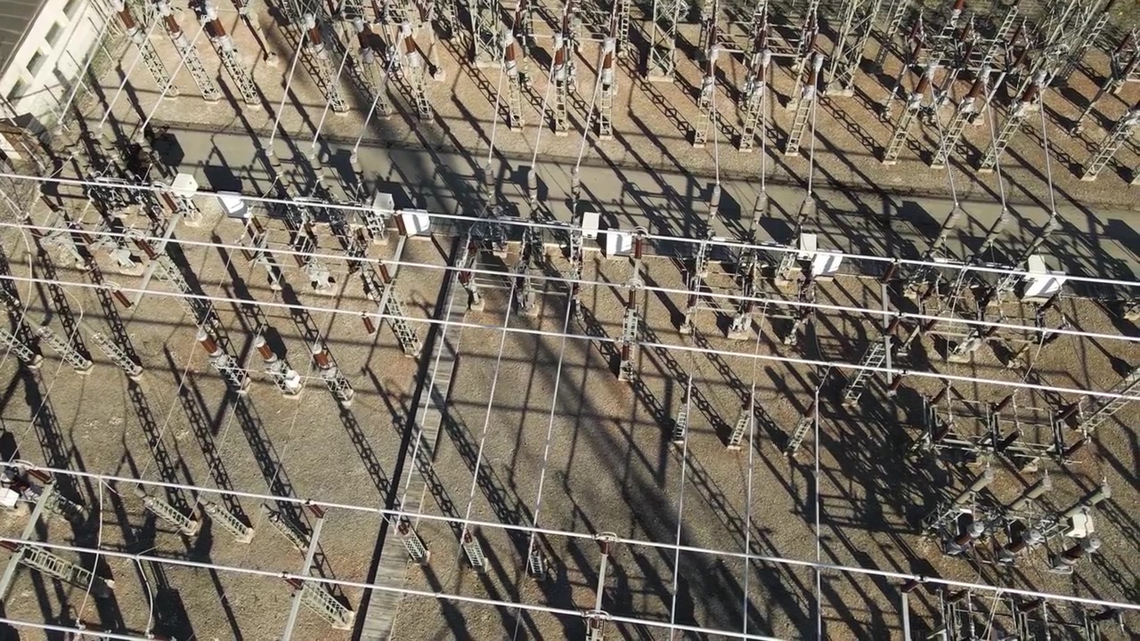High voltage electrical substation with a complex network of power lines, transformers, and switchgears generating and distributing electricity to the urban area on a sunny day with long shadows