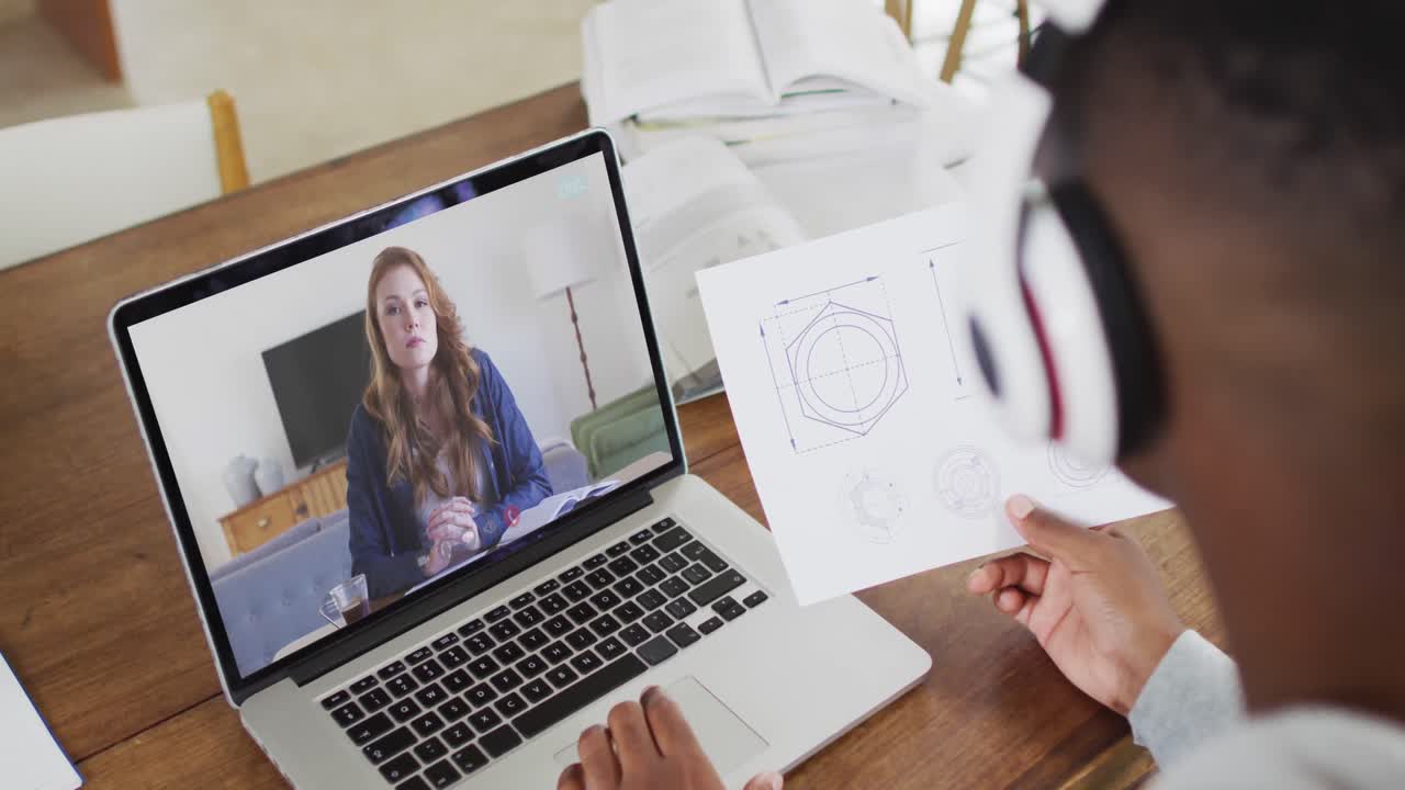 estudiante universitario afroamericano que sostiene notas mientras hace una videollamada en una computadora portátil en casa
