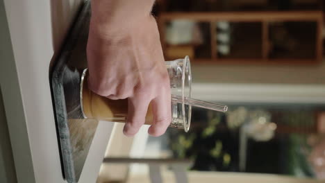 vertical video hand grabbing refreshing iced latte from the kitchen counter in slow motion close up homemade cold brew