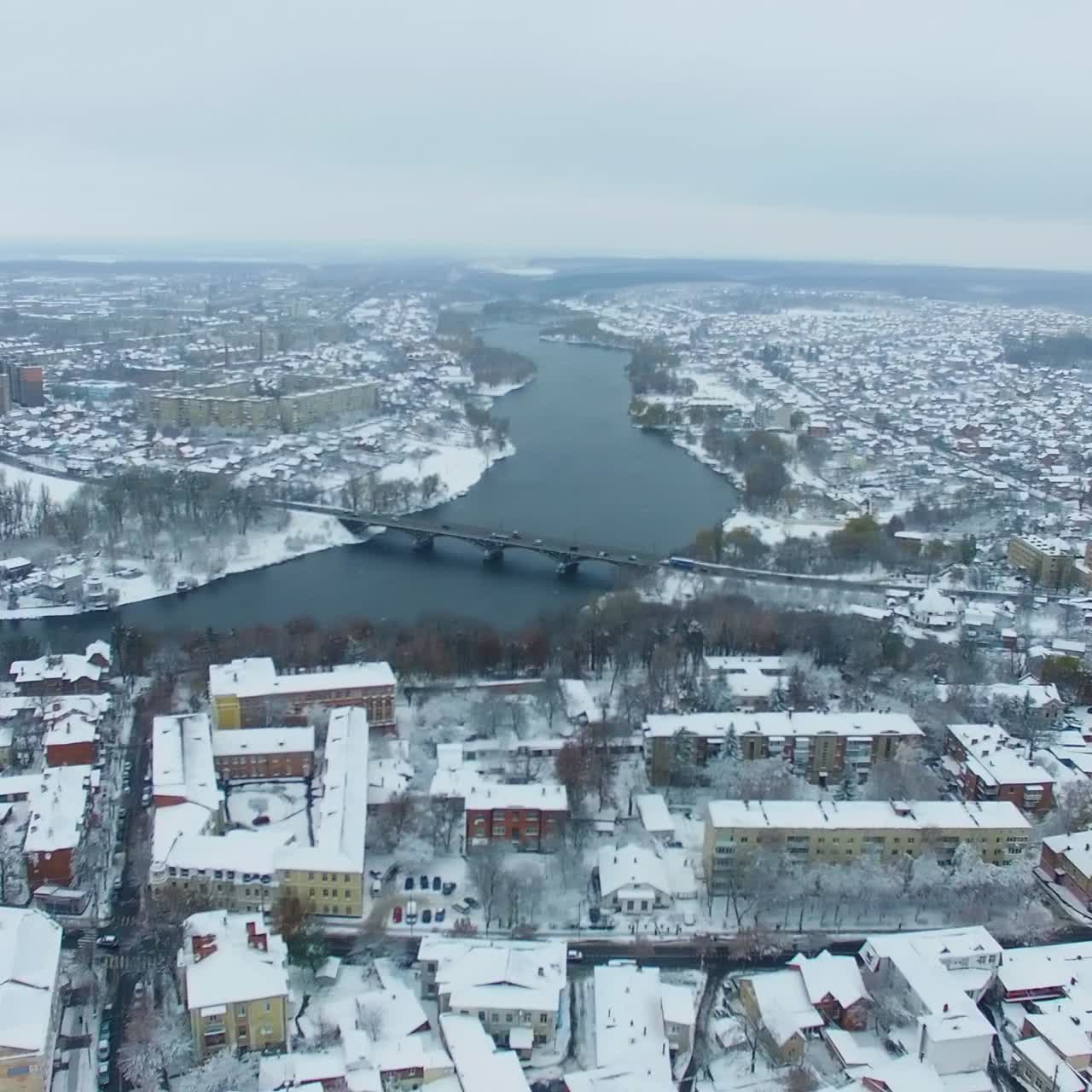 Twisted river diving the big city into two parts. Urban panorama on the cold gloomy snowy winter day. Top view