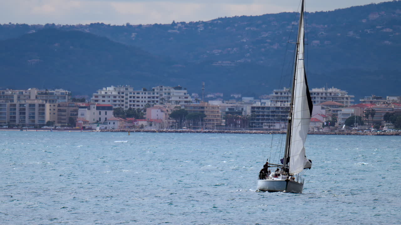 Sail boat moving on the sea in Juan-les-Pins, France with the city and the mountain on the background