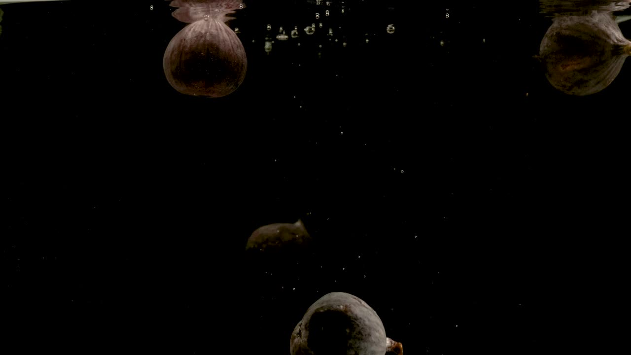 higos cayendo en el agua sobre un fondo negro. brillante video de alta calidad