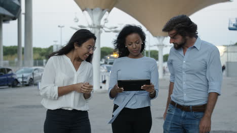 três colegas caminhando lentamente com um tablet e, em seguida, parados ao ar livre em um dia ventoso