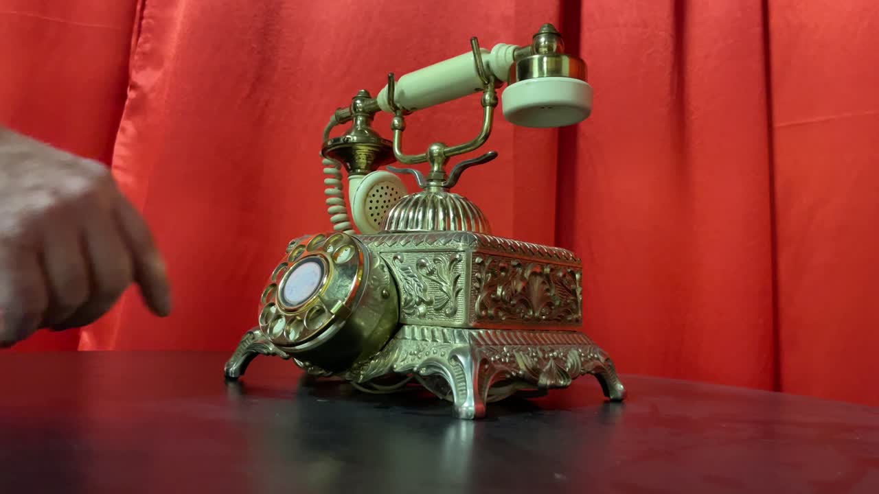 빨간색 커튼을 배경으로 금색의 오래된 골동품 로터리 전화를 손으로 다이얼링