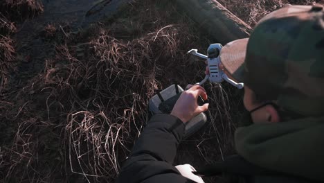 over the shoulder view of a person powering on his small dji mini drone uav quadcopter aircraft with grass sand mud logs in in the background