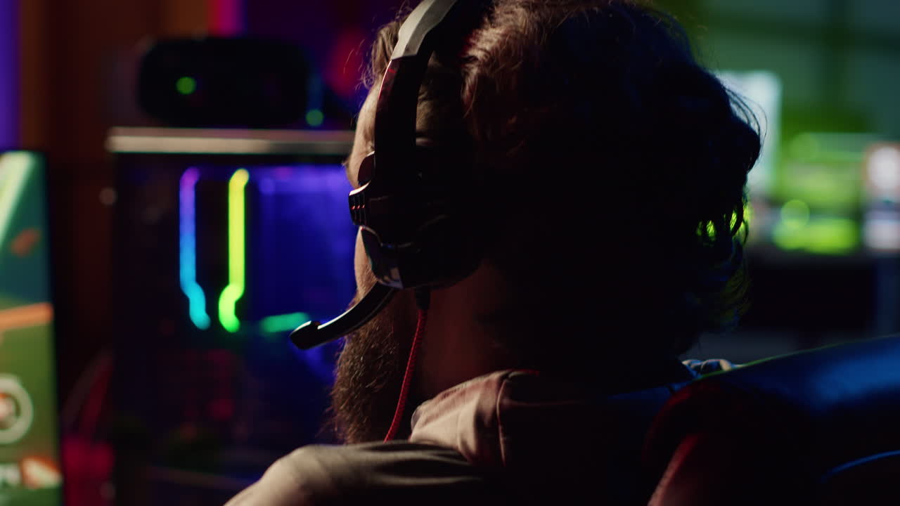 Gamer using headphones mic to talk with online friends from his dark living room, playing games