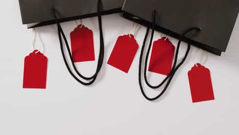 Two-black-gift-bags-with-five-red-sale-tags-on-white-background-with-copy-space