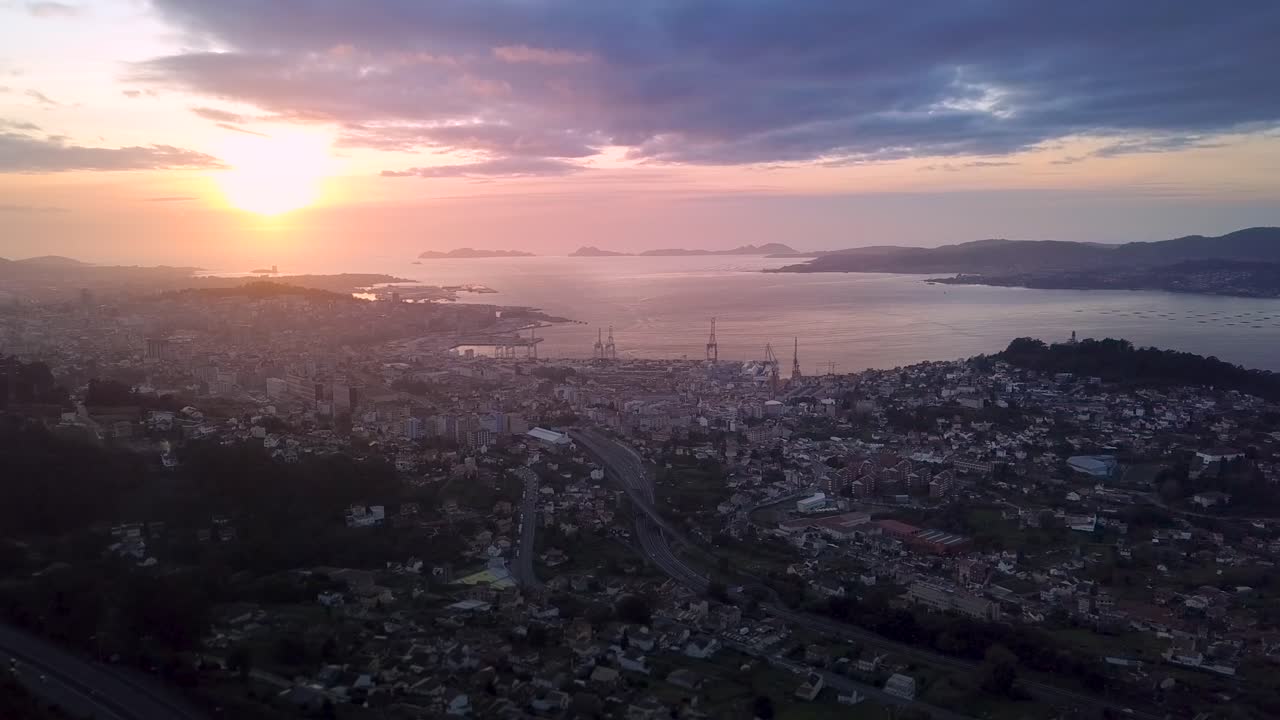 Aerial view of the industrial cityscape of Vigo at colorful sunset with the cranes of the harbour. Drone Stablishing shot with lateral travelling