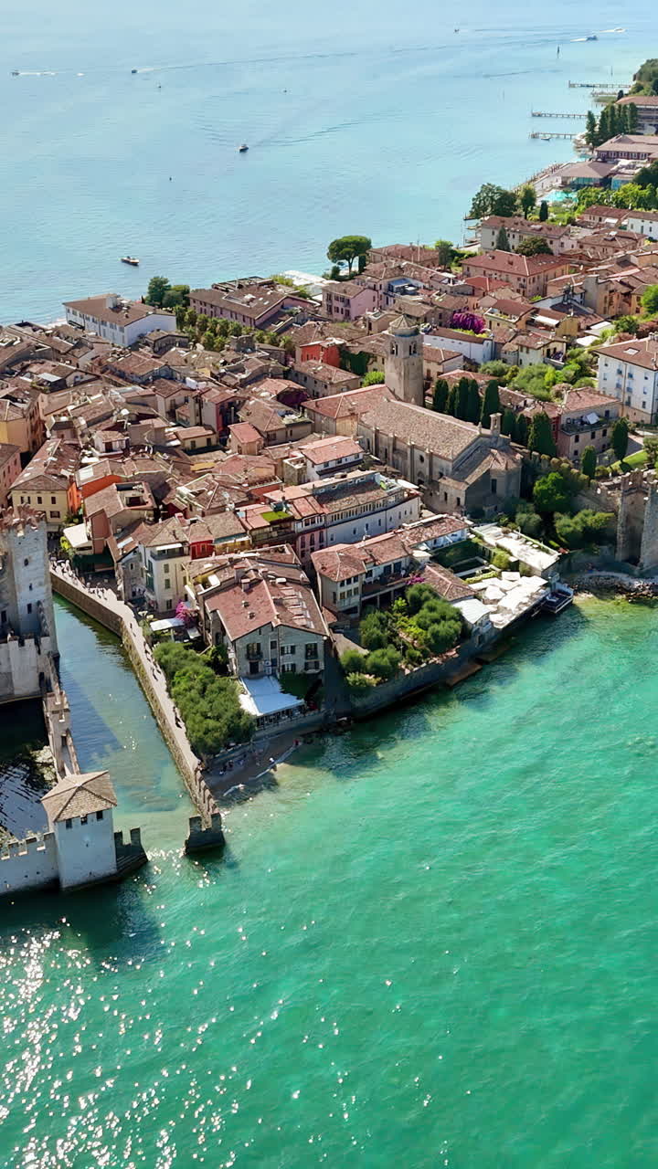 Dronebeeld van het Scaliger Kasteel in Sirmione, omringd door het turkooizen water van het Gardameer. Middeleeuwse muren en torens rijzen op boven de haven en de historische stad aan het meer. Verticaal.