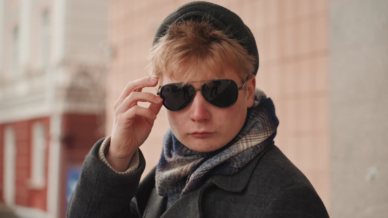 Sunglasses reveal caucasian creators stare, closeup urban portrait, hand lifts glasses, decisive expression and focused eyes, winter coat and scarf detail, candid editorial energy roles flow