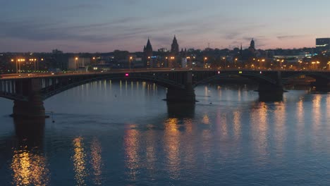 Sunset-aerial-drone-shot-of-the-city-of-Mainz-going-over-the-old-bridge-showing-the-Dome-in-the-heart-of-the-city-center-in-best-golden-hour-light-with-a-Drohne