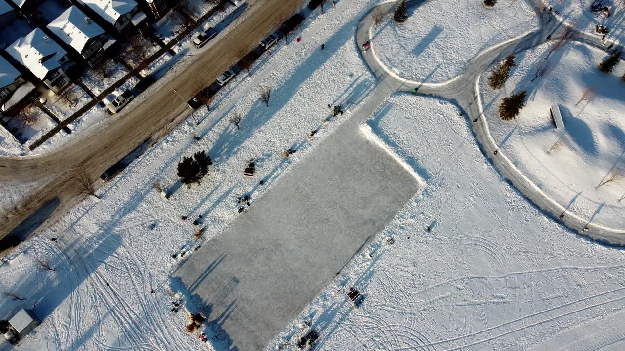 el ascenso aéreo invernal gira sobre viviendas unifamiliares residenciales en una pista de hielo artificial vacía y una pista ovalada doble donde la gente practica patinaje artístico y carreras en el parque comunitario junto a la carretera junto al parque infantil 3-3