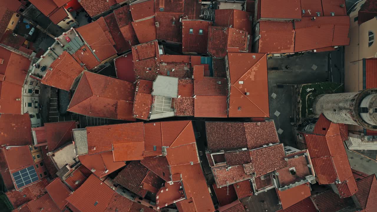 High altitude birdseye ascent over Ortonovo, Italy, layout of the historic dense village with flock of birds flying below