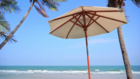 Tropical-Vacation-Scenery,-Beach-Parasol-Under-Palm-Trees-and-Blue-Ocean-Horizon