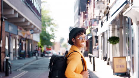 Back-view-of-fashionable-young-black-woman-wearing-a-hat-and-a-yellow-pea-coat-walking-in-the-street-and-turning-to-look-back-to-camera