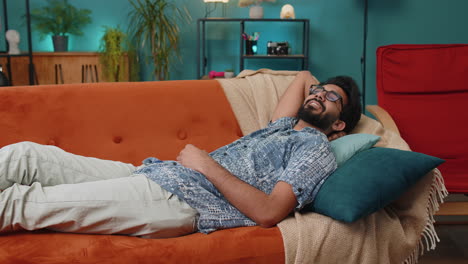tired indian man lying down in bed taking a rest at home napping falling asleep on sofa relaxing