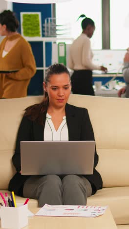 vertical video manager woman holding laptop, looking on internet while sitting on couch smiling
