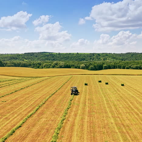beautiful scenery of the field near green forest in summer. agricultural tractor on the field at seasonal works. camera moves left. drone view.