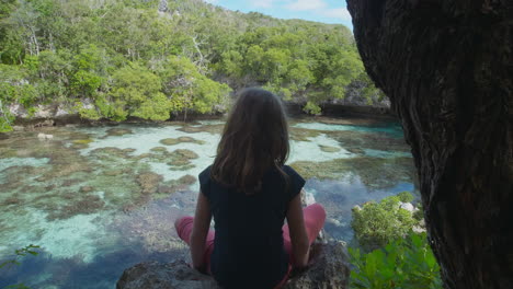 Girl-sitting-on-a-rock,-looking-on-corals,-in-shallow-waters-of-the-Loyalty-islands---tracking-view