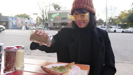 Cute-cool-Asian-woman-shaking-oregano-topping-on-her-margherita-cheese-pizza-at-outdoor-restaurant