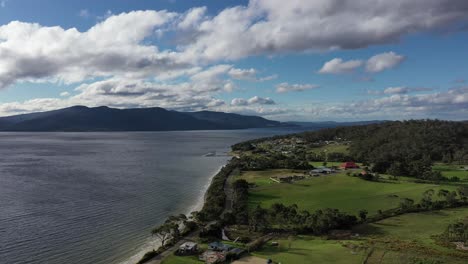 slow drone pan around small coastal town surrounded by blue water and green fields on sunny, cloudy autumn day