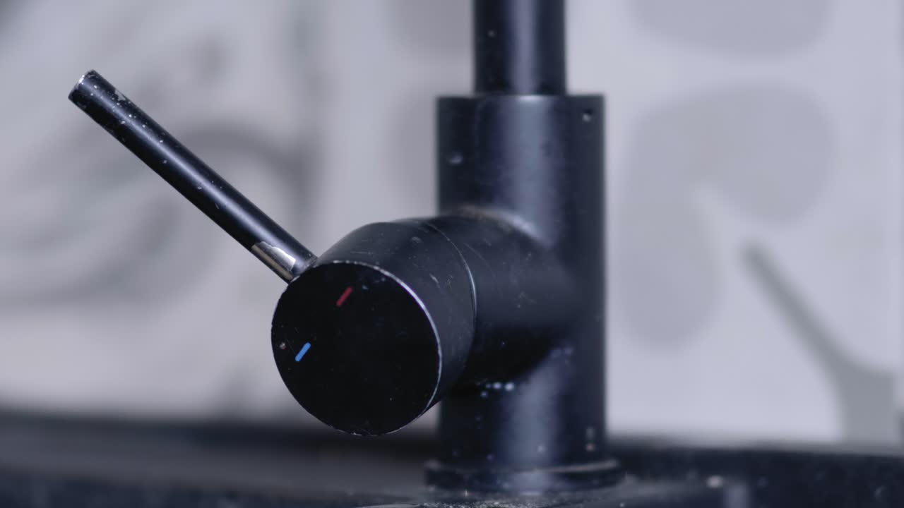 The cold water tap is turned on by a man's hand in a modern, grey kitchen.