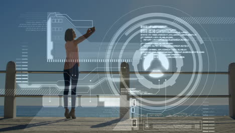 digital interface animation over person taking selfie by ocean railing