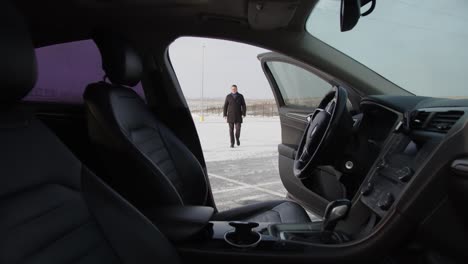 un hombre de negocios va a su coche en el estacionamiento en una calle nevada