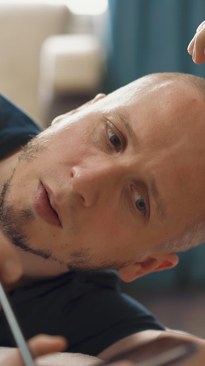 cu, tracking: young unshaven father shows little daughter student with long hair as prepare smartphone for distance learning, dad lies on floor, smiles